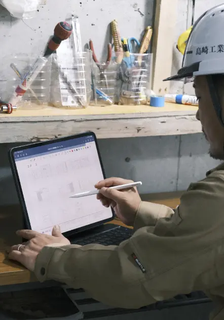 ヘルメットと安全眼鏡を着用した男性がノートパソコンで作業している様子