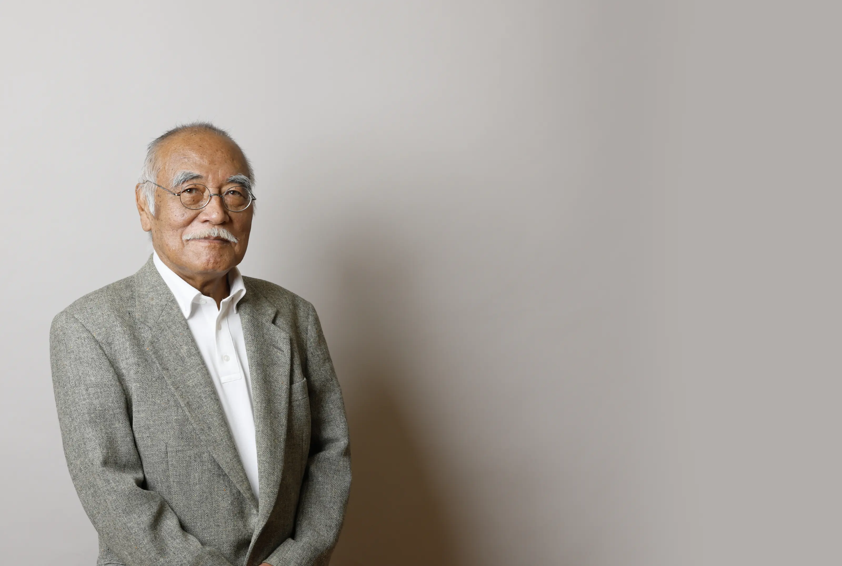 スーツとネクタイを着た年配の男性が壁に寄りかかって立っています。