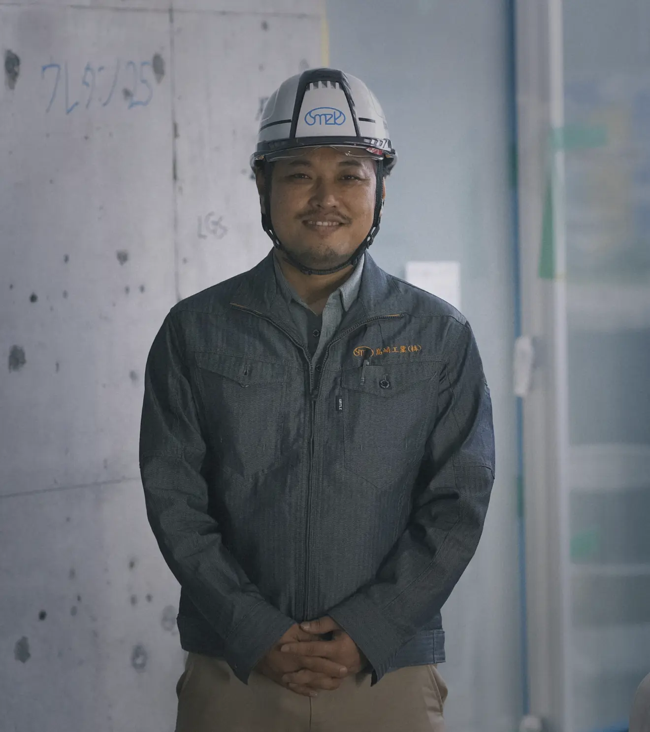 ヘルメットを着用し、正面を向いて穏やかに微笑む作業着姿の男性