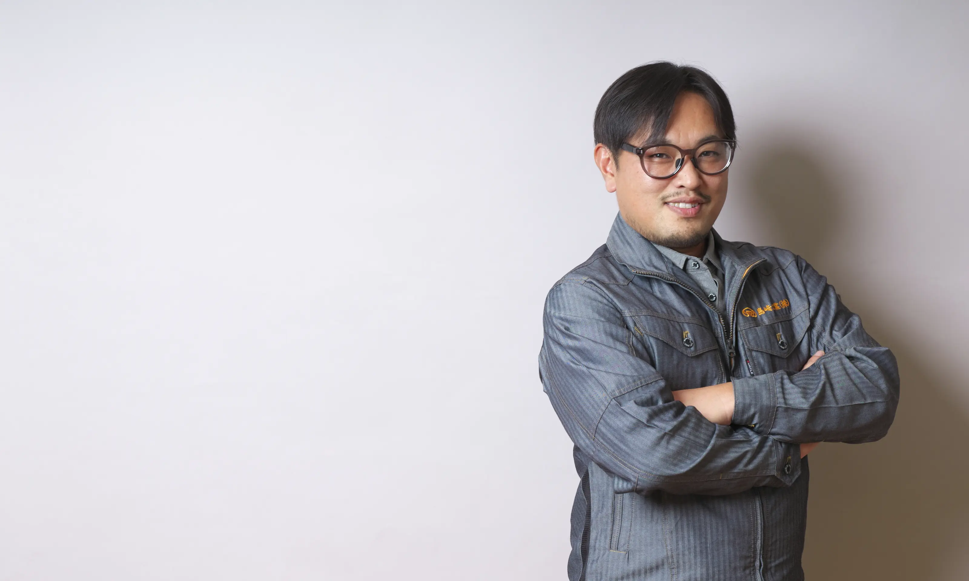 腕を組んで笑顔を見せる作業着姿の男性