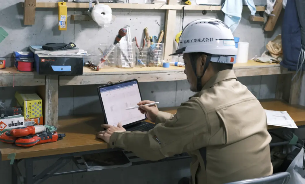 ヘルメットを着用し、デスクでタブレット端末を操作する作業員