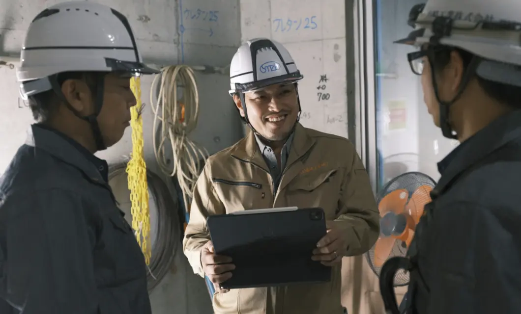 タブレットを手に、現場で打ち合わせを行うヘルメット姿の作業員たち