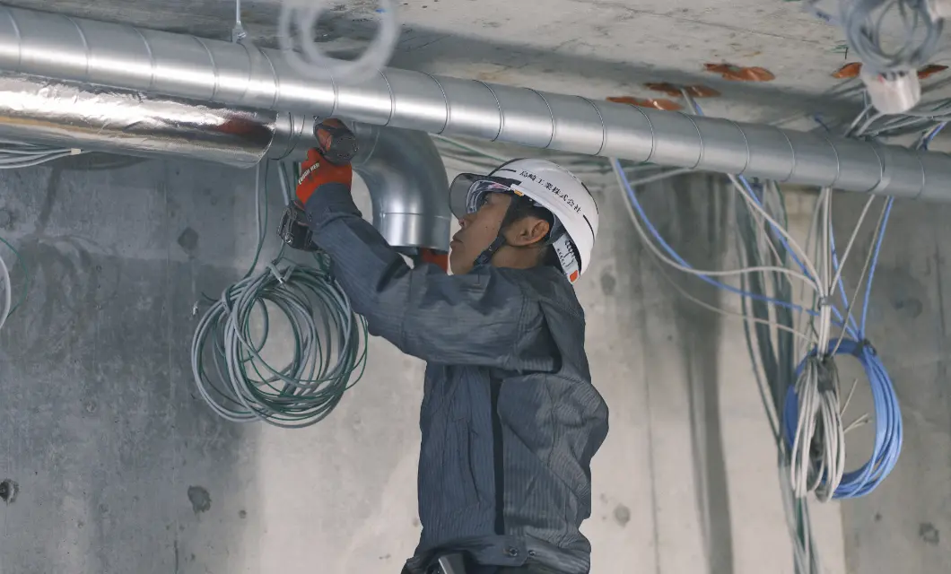建設現場で天井の配管工事を行う作業員
